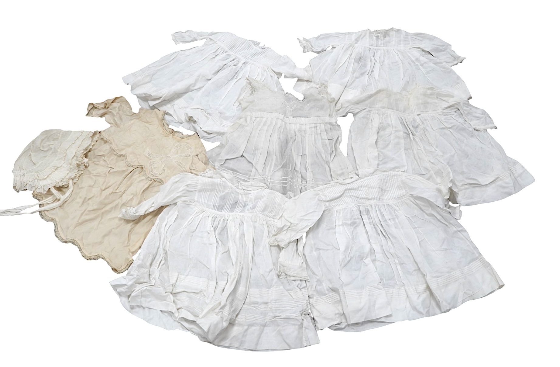 An early 20th century cream silk young girls day dress, together with six similar sized cotton and fine lawn day dresses and a bonnet, all dresses worked with tucking, feather stitching, some lace edged, the bonnet made